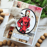 Card with the woman colored in a red coat, framed in a black circle with cheesecloth and beads.