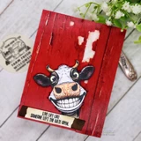 Red wood-grain card with the colored grinning cow, captioned 'Live life like someone left the gate open.'