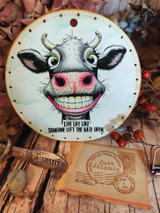 Round tag featuring the grinning cow with a pink nose, captioned 'Live life like someone left the gate open.'