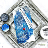 Deep blue speckled tag stamped “rudolph in a blizzard,” layered on a rustic silver frame with ink pads.