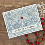Snowy gray-white speckled panel with a single red gem, stamped “rudolph in a blizzard,” styled with snowflakes and red berries.