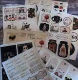 Assorted Halloween ephemera pieces spread out — ghosts, postcards, tags and word strips on aged kraft.