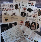 Assorted Halloween ephemera pieces spread out. Ghosts, postcards, tags and word strips on aged kraft.