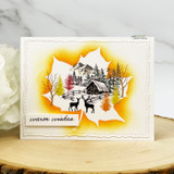 Card with the cabin scene glowing in an orange halo on a leaf, 'warm wishes' tag.