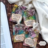 Grungy layered tags with scripture verses tied with ribbon over an open book.