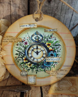 Round card with the clock and foliage in cool greens on a woodgrain background.