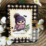 Black gingham card with a colored owl in a purple knit beanie on a branch and "you warm my heart"