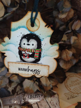 Wood ornament with the colored penguin and "warm hugs," surrounded by dried foliage