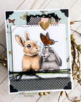 Card of two soft bunnies with a monarch butterfly over patterned papers, 'Welcome Spring.'