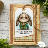 The robe-clad grumpy bunny on a kraft gift tag layered over plaid — 'World's Best Dad (when awake).'