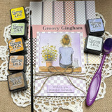 Groovy Gingham papers styled with a card of a girl sitting with a cat and a pot of daisies, laid out with distress ink pads and a blending brush on a doily.