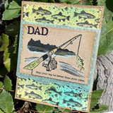 Kraft card with the fish background inked in green and blue, layered with a stamped fishing rod and lake scene and a small sentiment reading May your day be better than your jokes.