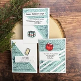 Three cards styled on a wood slice with greenery, in teal and kraft tones with a cellphone, a six pack and a cooler coloured small, and short funny dad sentiments on white strips.