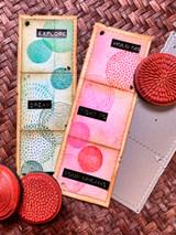 Two slim tags stamped with the circle designs in teal and pink with word tabs 'explore,' 'hold on,' 'your dreams.'