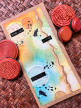 Card with the circle motifs over a rainbow ink-blended background with black splatter.