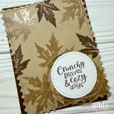 Kraft scalloped card with gold and white embossed leaves scattered across it, twine, and a white circle reading "Crunchy leaves & cozy days."