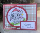 Card with the bunny colored grey in a red hat on a white circle over grey and red plaid paper, sentiment "Somebunny wishes you a Merry Christmas."