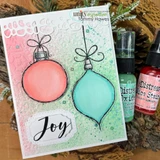 Card with the ornaments colored coral and aqua on a pink and mint stenciled background, with 'Joy' on a die cut label.