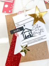 A white tag stamped with the nativity label reading ALL IS CALM ALL IS BRIGHT and WITH LOVE FROM, layered on kraft with a red glitter strip and two gold stars.