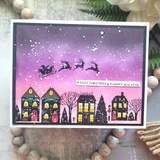 Card with the full village row stamped in black with glowing coloured windows against a purple and pink snowy sky, sentiment "A COZY CHRISTMAS & A HAPPY NEW YEAR."