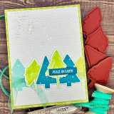 Christmas card with overlapping lime, teal and blue stamped pine trees on a grid background, tied with sheer ribbon and finished with a Peace on Earth banner.