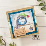 Kraft card with the bird colored soft blue in a purple knit hat, framed by a navy scalloped die cut, and a kraft tag reading "No distance can dim the warmth of Christmas love."