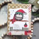 Card with the grey-brown bird in a red hat and red striped scarf over a black and white striped strip on a neutral panel, sentiment "No distance can dim the warmth of Christmas love."