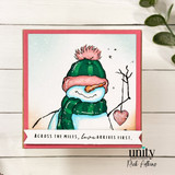 Snowman in a green hat on a soft pink card holding a heart with 'Across the miles, love arrives first.'