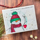 Snowman in a red-and-green hat and scarf on a wood-look card with die-cut snowflakes and 'Across the miles, love arrives first.'