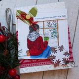 Card with the woman in a red sweater at a snowy window, 'a cozy Christmas & a happy new year.'