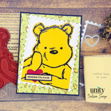 Bear holding a "Sending you a hug" banner beside a little book-of-love themed card in warm reds and golds.