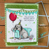 A stamped card showcasing a tired, hungover shaggy dog in a party hat slumped by a balloon and gift from Unity Stamp Co's Party Pup red rubber stamp set, with the sentiment 'You survived another year of bad decisions.'.