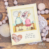 Soft yellow card of the couple watching the sea, framed in stitched cream with a pink heart and the forgotten the year but not each other sentiment, styled on shells and a lace doily.
