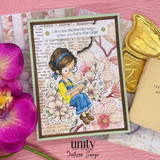 Handmade card made with Unity Stamp Co’s Once the Story Opens red rubber stamp set — a bespectacled girl with an updo sitting reading a book among blooming flowers — stamped and colored, with the sentiment “Life’s best moments begin when you turn the page”.