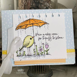 Card with a yellow bird under an orange umbrella over dotted papers and 'Rain makes room for things to bloom.'