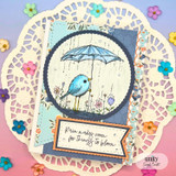 Doily card with the bird under an umbrella on a circle with flowers and 'Rain makes room for things to bloom.'