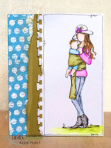 Tall card with a blue polka-dot and gold panel beside Stella Girl coloured in pink, teal and grey, holding her baby against a white background.