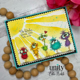 Sample card on wooden beads. A yellow sunburst background flecked with teal splatter sits behind five fuzzy long legged birds with wide eyes, framed in teal and black zigzag borders.