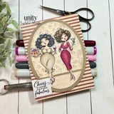 Card sample using the Scallops & Ovals nesting die frame: a scallop-edged oval mat cradles two glamorous cartoon women toasting with wine and a martini on a pink-striped panel, with the sentiment "Cheers to another year of being fabulous."