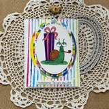 Scallops & Ovals die frame on a birthday card, a stitched oval mat over a rainbow-striped panel holding a smiling snail that carries a wrapped gift, captioned "I remembered. The card was slow."