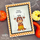 Highland cow in a ghost sheet with its jack-o'-lantern bucket on a cream panel with orange gingham border, 'Happy hauntings.', surrounded by real pumpkins.