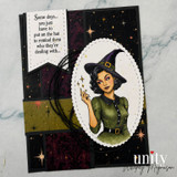 Black and gold Halloween card with a colored witch in a green dress and pointed hat in a scalloped oval frame on a starry night background, with the sentiment 'Some days... you just have to put on the hat to remind them who they're dealing with...'