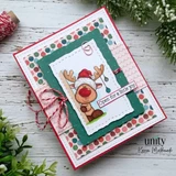 Card with a green deckled frame and polka dot and scallop papers, the reindeer peeking around a post in a glittery Santa hat with ornaments hanging from his antlers, tied with red and white twine and a small sentiment strip.