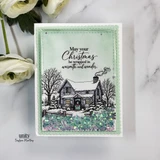 Shaker card with a mint scalloped frame and sparkly star confetti: the snow-covered cottage with a wreath on the door, lit windows, chimney smoke and bare trees in soft grey, under 'May your Christmas be wrapped in warmth and wonder.'