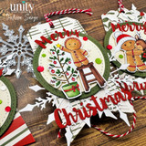 Close up of a Baking Spirits Bright gift tag from Unity Stamp Co: the gingerbread boy on a brown wooden stool placing a yellow star on a little potted tree hung with red baubles and a red bow, on a cream circle in a green scalloped frame with a red Christmas die cut below.