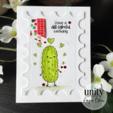 Scalloped postage-stamp frame card on white: the smiling green pickle with stick arms, surrounded by tiny green hearts and red sequins, with the sentiment 'Have a dill-ightful birthday.' in the corner.