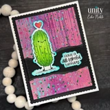 Card with a black scalloped frame over hot pink and purple distressed background with green splatters: the smiling green pickle with stick arms and legs and a red heart above, beside the sentiment "Have a dill-ightful birthday."