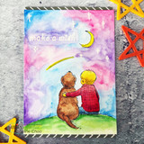 Card with the boy and dog on a green hill under a pink, blue and purple watercolor sky with white stars, 'make a wish' in white lettering, styled with orange star embellishments.