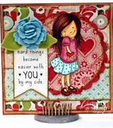 Card with the girl in a pink top and aqua dotted skirt against a red lace doily on floral paper, with a blue felt rose and a pennant banner.