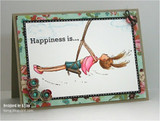 Kraft card with a floral and dotted border, a white panel holding the hand colored swinging girl in a pink skirt, with Happiness is... stamped at the upper left.